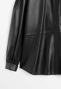 Chemise à manches longues en similicuir noir avec fermetures à boutons, poignets froncés et un détail de couture traversant la poitrine et les manches.