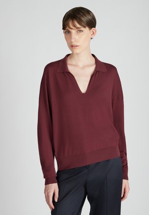 Bordeaux lange mouwen pullover met een diepe V-hals en geribbelde zoom; zachte textuur; gedragen met donkere, op maat gemaakte broeken.