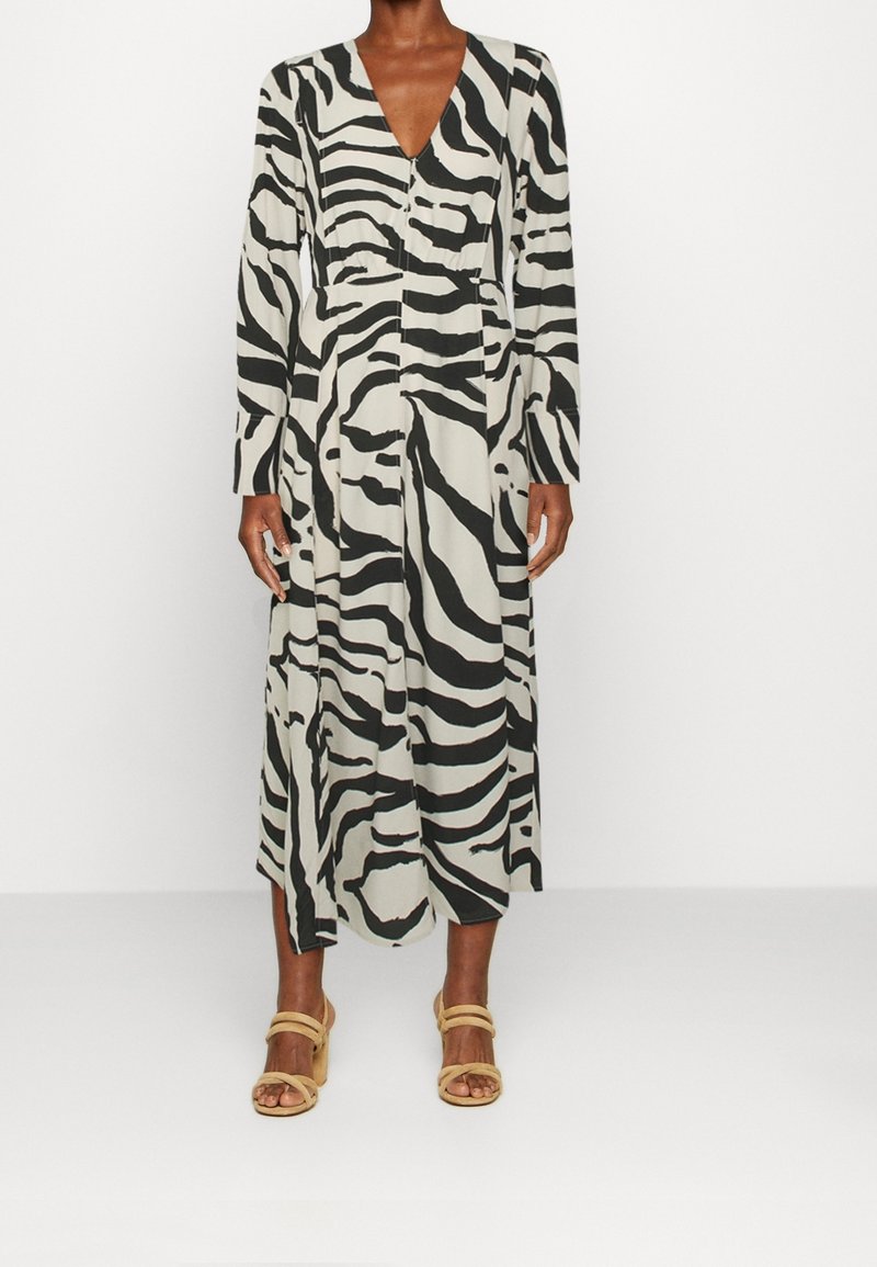 Robe à manches longues et encolure en V avec un imprimé zèbre noir et blanc. Tissu fluide avec une taille cintrée et une jupe mi-longue. Sandales à talons carrés.