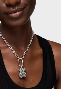 Collana in argento con pendente a forma di orso e testo nero. La catena è composta da link rotondi, con una finitura liscia e una texture lavorata.