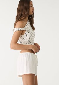 Top blanc à pois avec des épaules dénudées et un corsage ajusté, associé à un short blanc à cordon de serrage, mettant en valeur un tissu doux et décontracté.