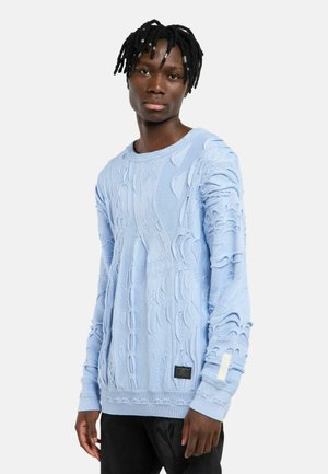 Lyseblå strikket sweater med teksturerede mønstre, rund halsudskæring og ribstrikkede manchetter. Inkluderer et mærke med brand på nederste venstre side.
