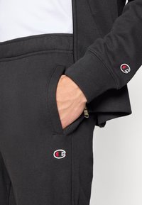 Μαύρο φούτερ με ελαστικές μανσέτες και μέση, με μικρό κεντημένο λογότυπο. Περιλαμβάνει πλαϊνή τσέπη και λεπτομέρεια με φερμουάρ στο μπουφάν.