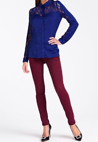 Blouse bleu marine avec manches en dentelle, design à boutons. Associée à un pantalon skinny bordeaux et des talons hauts noirs avec des embellissements.