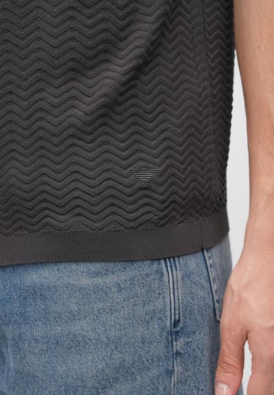 Sveter s krátkym rukávom v tmavošedej farbe s textúrou a cikcak vzorom, so žebrovaným lemom. Kombinovaný s nohavicami z svetlomodrého denimu.