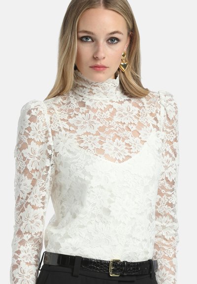 Witte kanten blouse met een hoge hals, bloemmotieven, doorzichtige lange mouwen en een gestructureerde afwerking, gedragen met een zwarte riem.