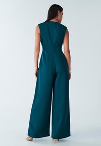 Tiefseeblauer Overall mit figurbetontem Oberteil, weitem Bein und ärmellosem Design. Mit verdecktem Reißverschluss auf der Rückseite und glatter Textur.