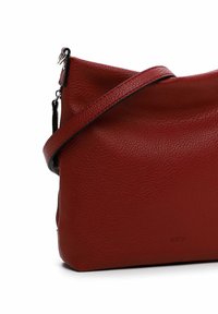 Sac à main en cuir rouge avec une finition texturée, design en diagonale, bandoulière ajustable et une discrète marque sur le devant. Fermeture éclair sur un côté.