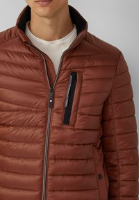 Bruine winterjas met horizontale stiksels, hoge kraag en een ritsvak op de borst. Het materiaal is glad met een lichte glans.