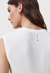 T-shirt bianco in cotone con maniche corte arrotolate, caratterizzato da un logo nero sulla parte posteriore del colletto e una texture liscia e morbida.