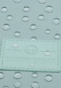Vízálló, mentaszínű anyag, vízcseppekkel, világoskék, domború feliratú címkével, amelyen a "JOHNNY URBAN" felirat olvasható. Strukturált felület.