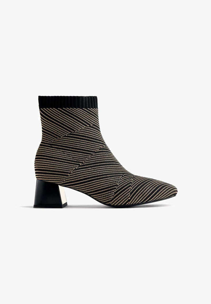Bottines à rayures noires et dorées avec une tige en tricot, un bout pointu et un talon épais noir avec un détail métallique.