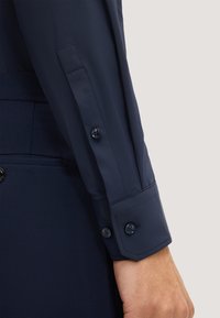 Marineblauwe shirtmouw gemaakt van een gladde, lichte stof met knopen bij de pols en een getailleerde manchette. Heeft een subtiele textuur en strakke lijnen.
