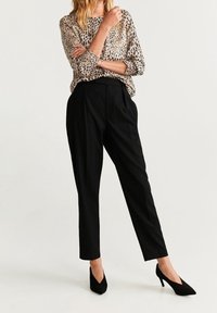 Beige Bluse mit Leopardenmuster, lockere Passform, lange Ärmel. Schwarze hochtaillierte Hose, schmal geschnitten, glatte Textur. Schwarze spitze Absätze.