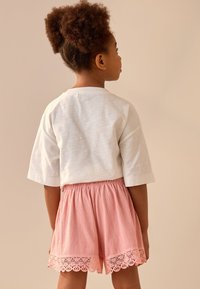 Bílá košile s krátkým rukávem a kulatým výstřihem spojená s růžovými texturovanými šortkami s krajkovou lemovkou na lemu. Jednoduchý design, volný střih.