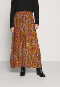 Gonna maxi in tessuto arancione a fantasia con motivi floreali. Forma a trapezio con una finitura testurizzata, abbinata a stivali neri alla caviglia.