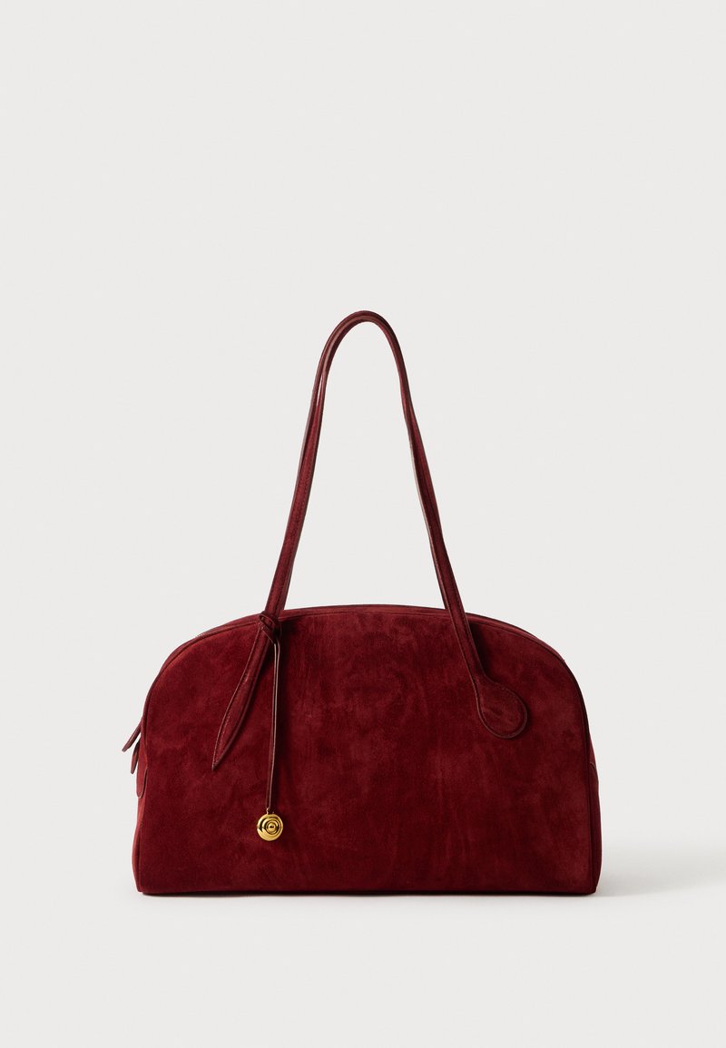 Borsa a tracolla in suede bordeaux con due manici arrotondati, un dettaglio accentuato in oro e una texture liscia. Il design è spazioso e dolcemente curvato.