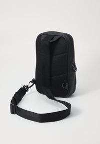 Borsa nera con un design in rete texurizzata, chiusura a zip e tracolla regolabile. Forma rettangolare compatta con accenti minimalisti.
