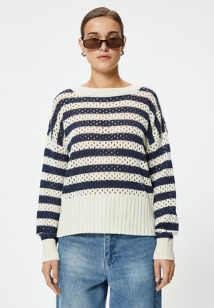 Gebreide trui met verticale strepen in marineblauw en crème, met een losse pasvorm, ribgebreide zoom en openweefdesign. Gecombineerd met lichtblauwe jeans.
