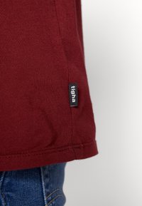 Marron kortærmet T-shirt lavet af bomuld, med et side søm label og en glat tekstur med en lige kant.