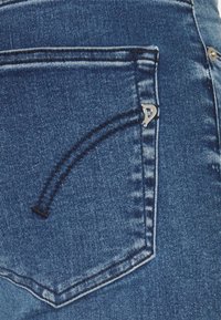 Vaqueros de mezclilla con un lavado azul oscuro, costuras de bolsillo curvadas y un acento de hardware plateado cerca del bolsillo para un detalle adicional.