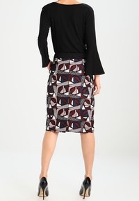 Czarna bluzka z długim rękawem i ołówkowa spódnica w geometryczne wzory w kolorach bordo, kremowym i niebieskim, o gładkiej fakturze i dopasowanym kroju.