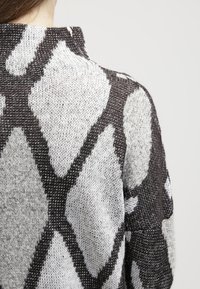 Maglione lavorato a maglia con un design a motivi. Presenta forme a diamante grigie e bianche alternate, un tessuto testurizzato e un collo alto.