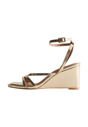 Gold and beige wedge sandal with crisscross straps, ankle strap, textured faux leather, and a wedge heel design. Smooth finish and light wood sole.
