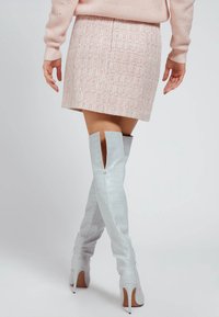 Vaaleanpunainen tweed-hame, jossa on hienovarainen tekstuuri, yhdistettynä yli polven kiiltävän vaaleanharmaisiin saappaisiin, joissa on krokotiilikuosi ja korkeat korot.