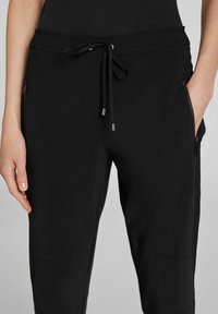 Joggers negros con cintura ajustable, bolsillos laterales con cremallera y una textura suave y lisa. Presentan un corte ajustado y un diseño minimalista.