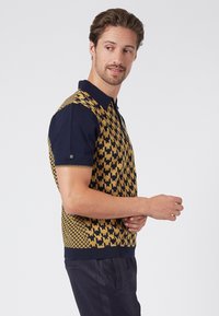 Short-sleeve polo shirt featuring a yellow and navy houndstooth pattern, with a ribbed collar and hem. Made of textured fabric.