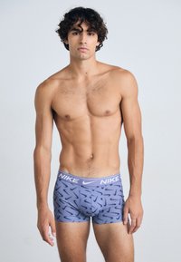 Grå boxershorts med et repeterende mørkeblå swoosh-mønster, som har en bred elastisk linning med "NIKE"-merke i hvitt.