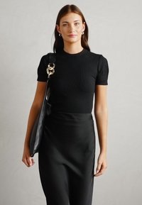 Top corto a righe nero a maniche corte abbinato a una gonna midi nera in satin. Modella porta una borsa in pelle nera con dettagli in oro.