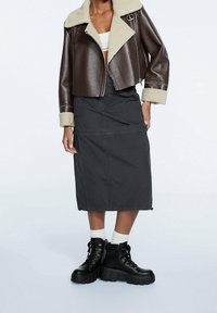 Brązowa krótka kurtka z imitacji skóry ze kołnierzem z futerka, zestawiona z czarną midi spódnicą i masywnymi czarnymi botkami na sznurowadła.