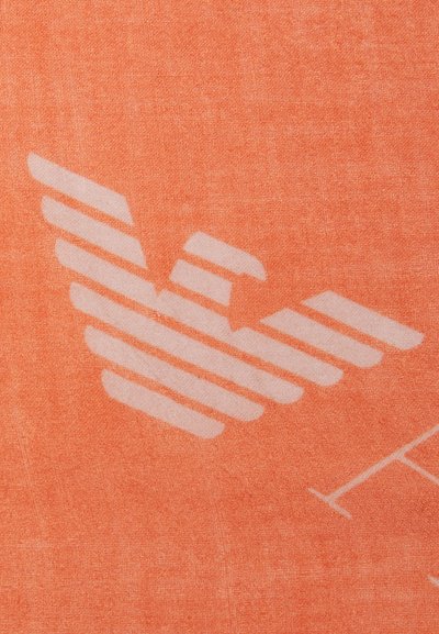 Orange textil med en stor, vit grafik av stiliserade vingar med horisontella ränder, mot en texturerad bakgrund.
