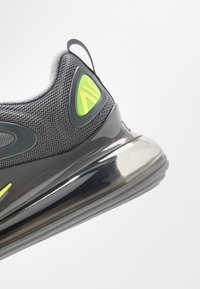 Šedá sportovní bota s prodyšným svrchním materiálem, zelenými akcenty a lesklou černou vzduchovou podrážkou. Obsahuje poutko pro snadné nazouvání.