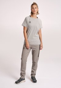 Grijze sport t-shirt met zwarte accenten, gecombineerd met lichtgrijze broek met zijstrepen en enkeldetails. Zwarte sneakers maken de look af.