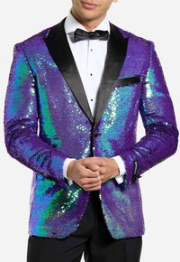 Blazer viola con paillettes e riflessi iridescenti, rever in raso nero e una tasca sul petto, indossato sopra una camicia bianca con cravatta a farfalla.