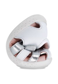 Zapato de cuero blanco con acentos metálicos plateados. Presenta un diseño redondeado y suave, cortes para la transpirabilidad y una suela flexible con perforaciones.