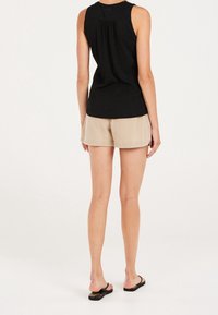 Czarny top bez rękawów o fakturowanej tkaninie, w połączeniu z beżowymi szortami. Sandały mają czarną podstawę i wielokolorowe kwiatowe akcenty.