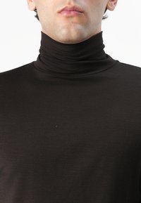 Fekete garbó, könnyű anyagból készült, szoros illeszkedésű és sima tapintású, rétegezéshez ideális.