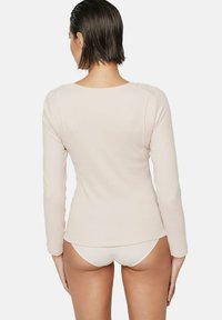 Haut rose clair à manches longues fabriqué en tissu doux, avec un col arrondi et un design ajusté, montré de dos avec des sous-vêtements assortis.