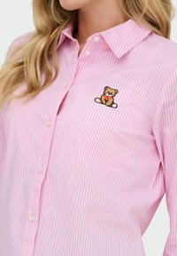 Camisa abotonada a rayas rosas y blancas con un bordado de un oso de peluche en la parte izquierda del pecho. Hecha de un tejido de algodón ligero.