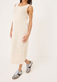 Kremowa sukienka dzianinowa sięgająca do kolan z szerokimi ramiączkami, z fakturowanej tkaniny, w zestawieniu z szaro-srebrnymi tenisówkami z akcentem w zwierzęcy wzór.