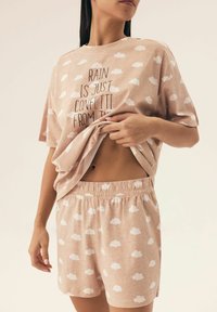 Jasnoróżowy zestaw piżamowy z bawełny, zawierający bluzkę z krótkim rękawem z wzorem chmur i napisem oraz szorty z elastycznym pasem i nadrukiem chmur.