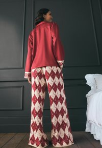 Rote Langarmjacke mit gemusterten Ärmelbündchen, kombiniert mit cremefarbenen, weiten Hosen, die mit einem roten diamantförmigen Muster und dezenten Designelementen versehen sind.