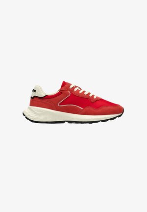Zapatilla deportiva roja con cordones blancos, suela blanca acolchada, suela exterior negra y lengüeta beige en el talón con detalle de marca en negro.