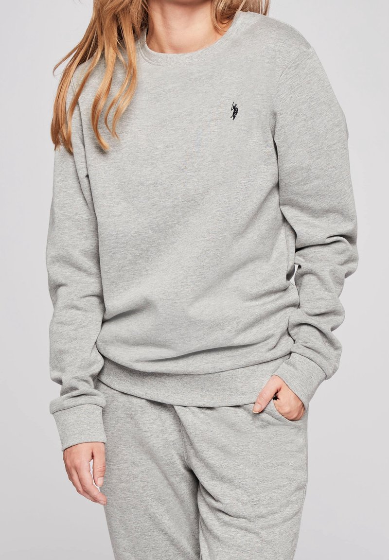 Sweat-shirt gris clair en tissu doux, avec un col rond, des poignets côtelés et un petit logo noir sur la poitrine.