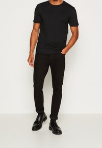 Černé tričko s krátkým rukávem v kombinaci s černými úzkými džíny a černými botami. Oblečen í má jednoduchý design s hladkou texturou.