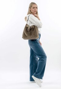 Borsa in pelliccia sintetica beige con chiusura a coulisse, accessori in argento e un portachiavi decorativo. Abbinata a jeans azzurri chiari e scarpe da ginnastica bianche.